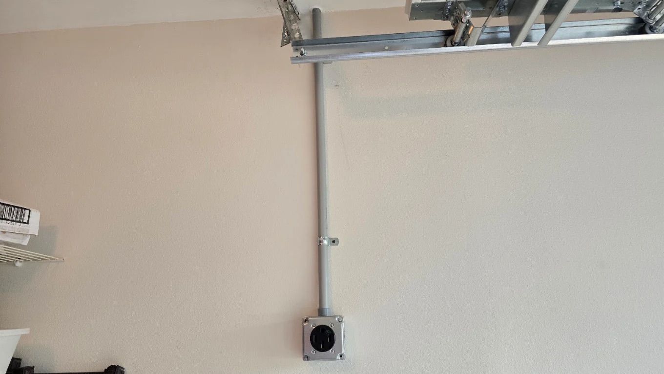 White wall with mounted garage door track and a small outlet box near the floor.