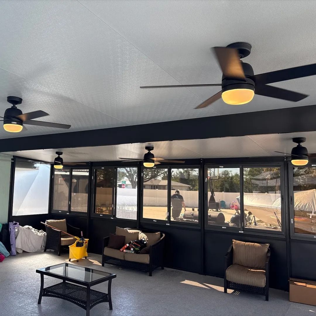 Covered patio with black ceiling fans, seating, and large windows overlooking a yard