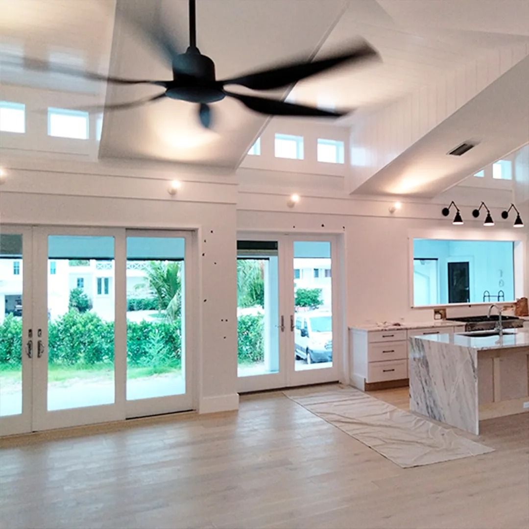 Bright open kitchen-living room with large glass doors, white cabinetry, marble island, and ceiling fan