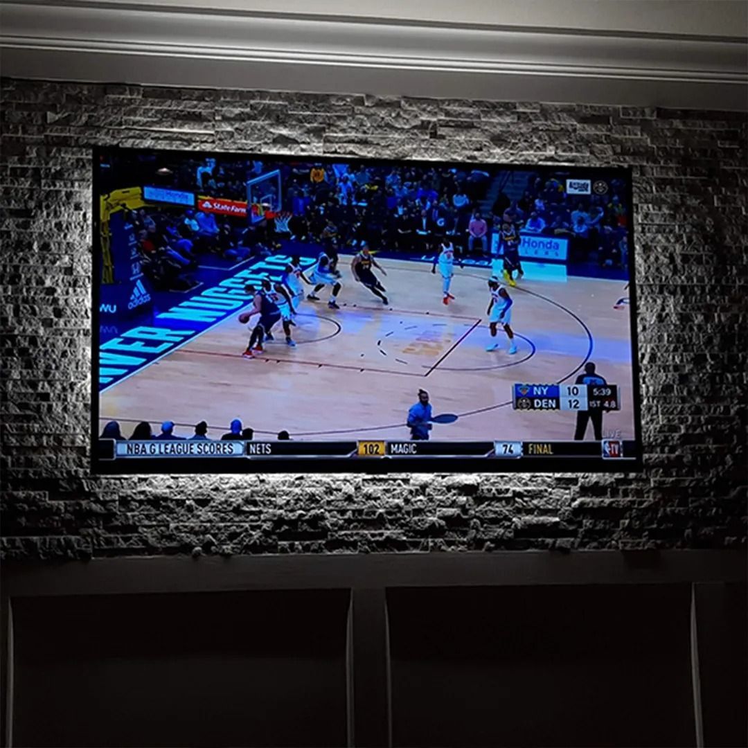Wall-mounted TV showing a basketball game in a dim room with stone accent wall.