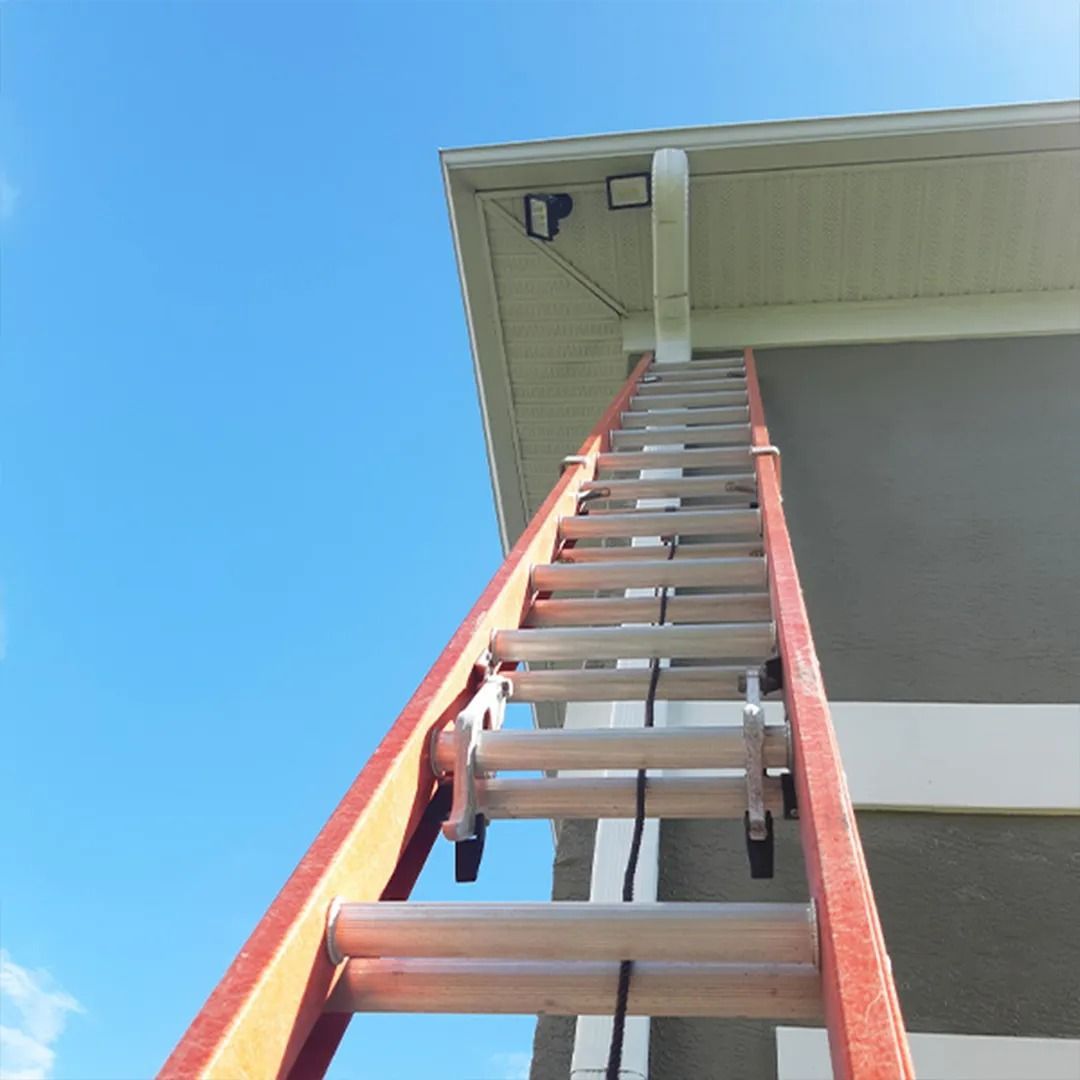 Red ladder leaning against house eave against a blue sky