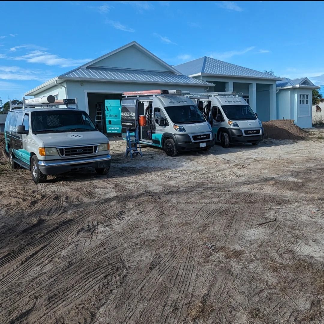 Two white service vans parked outside a newly built house on a dirt lot under a blue sky