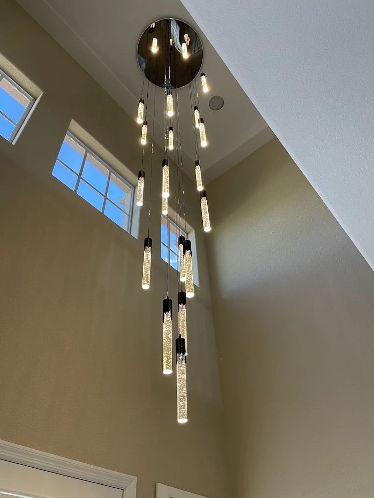 Modern chandelier hanging in a tall beige room with large windows and a vaulted ceiling