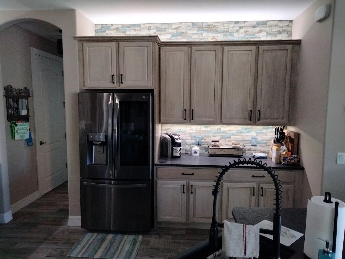 Kitchen with black refrigerator, light wood cabinets, and a tiled backsplash.