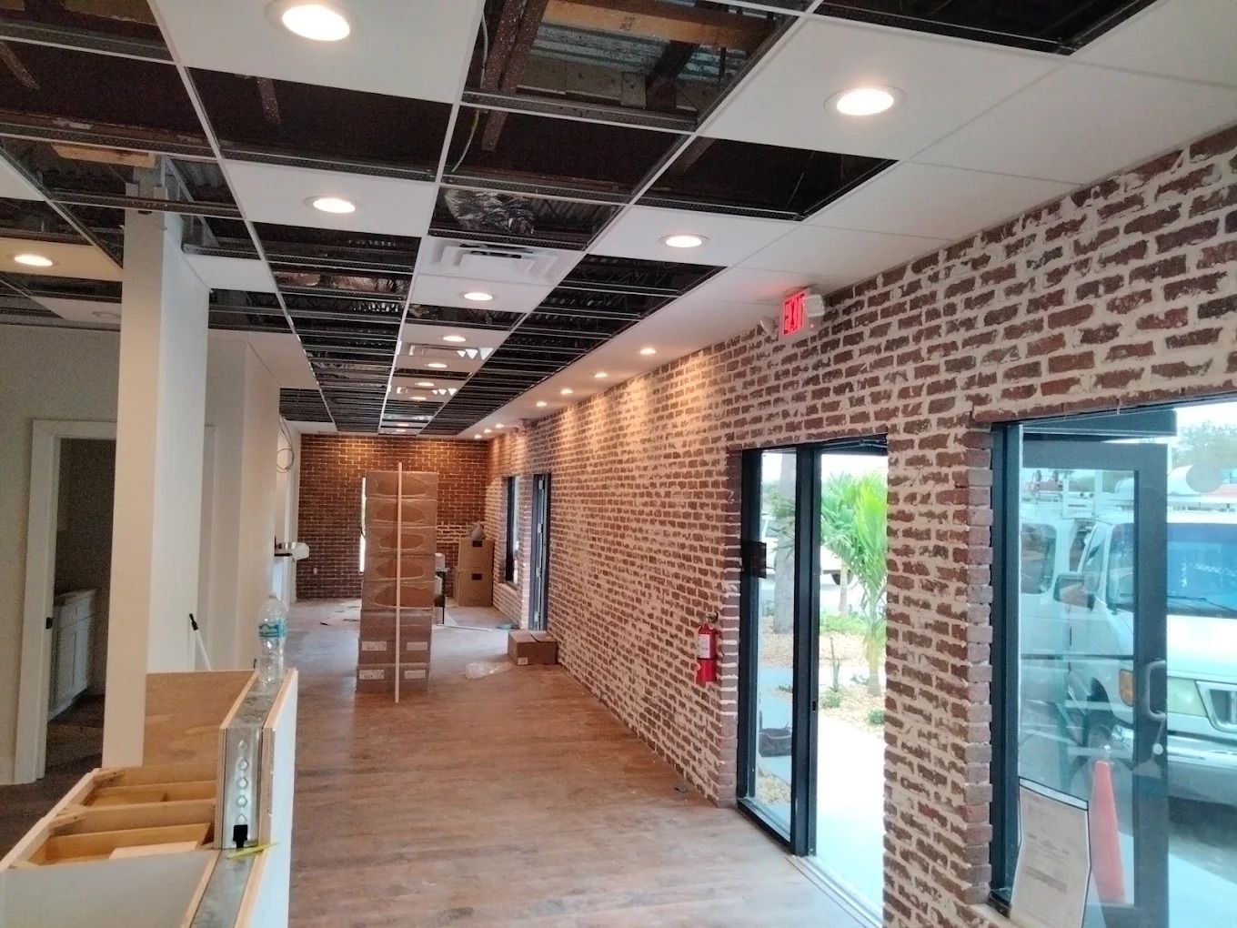 Renovated hallway with brick walls, wood floor, and ceiling tiles missing in a partially finished interior.