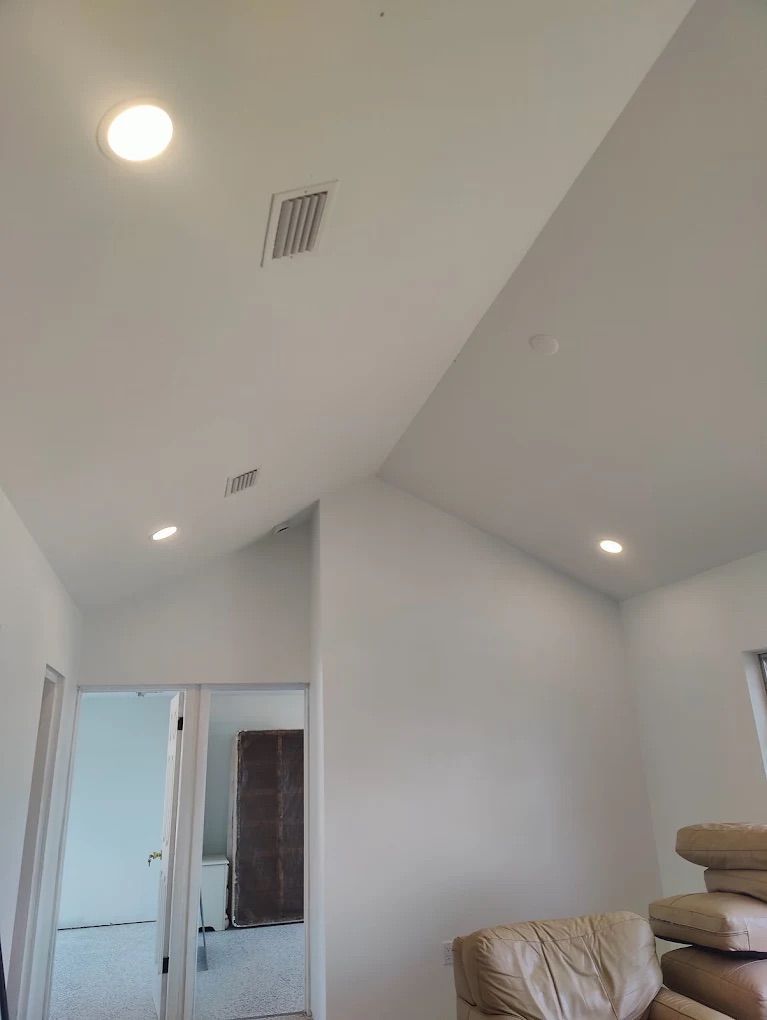 Bright attic bedroom with white sloped ceilings, recessed lights, and a beige bed in the corner