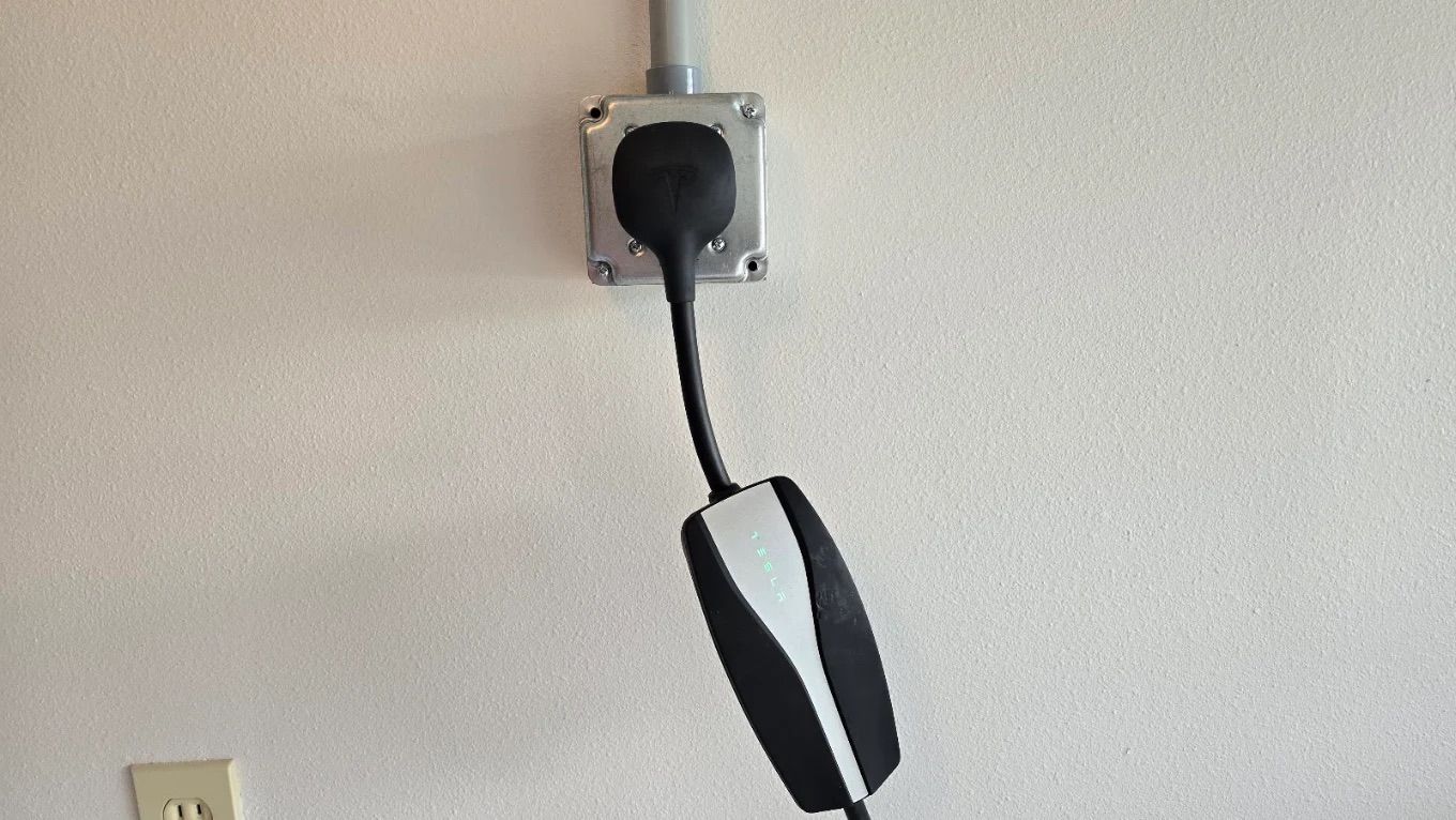 Black plug hanging from a wall outlet with a looped cord on a beige wall