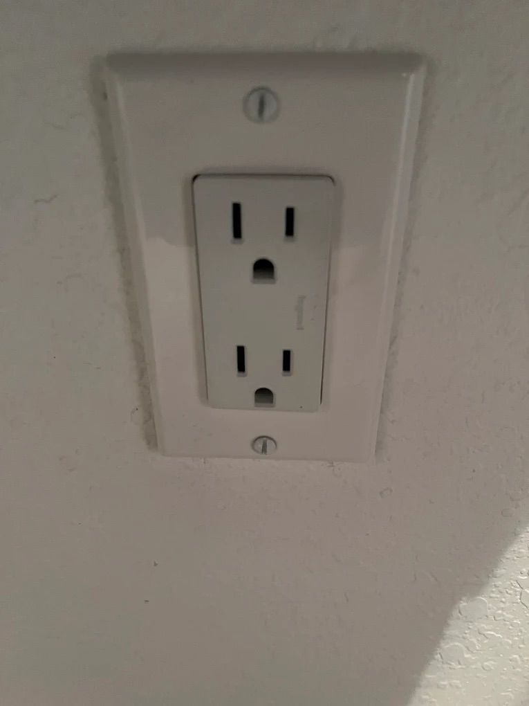 White duplex electrical outlet on a light wall plate against a beige wall.