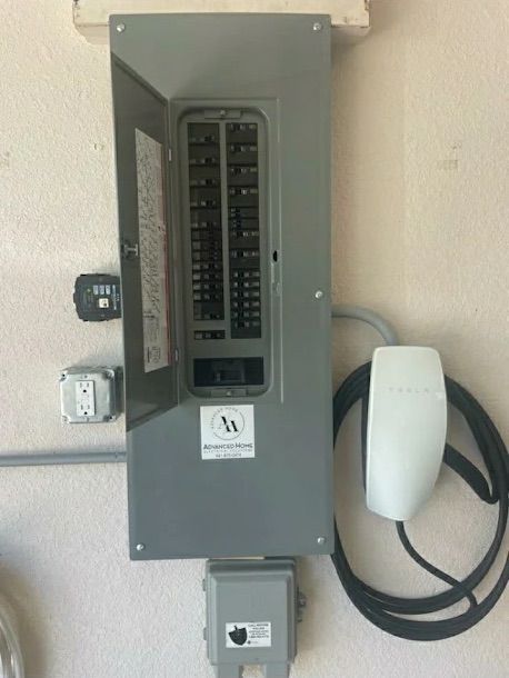 Open electrical breaker panel on a wall with a small white device and coiled cable beside it