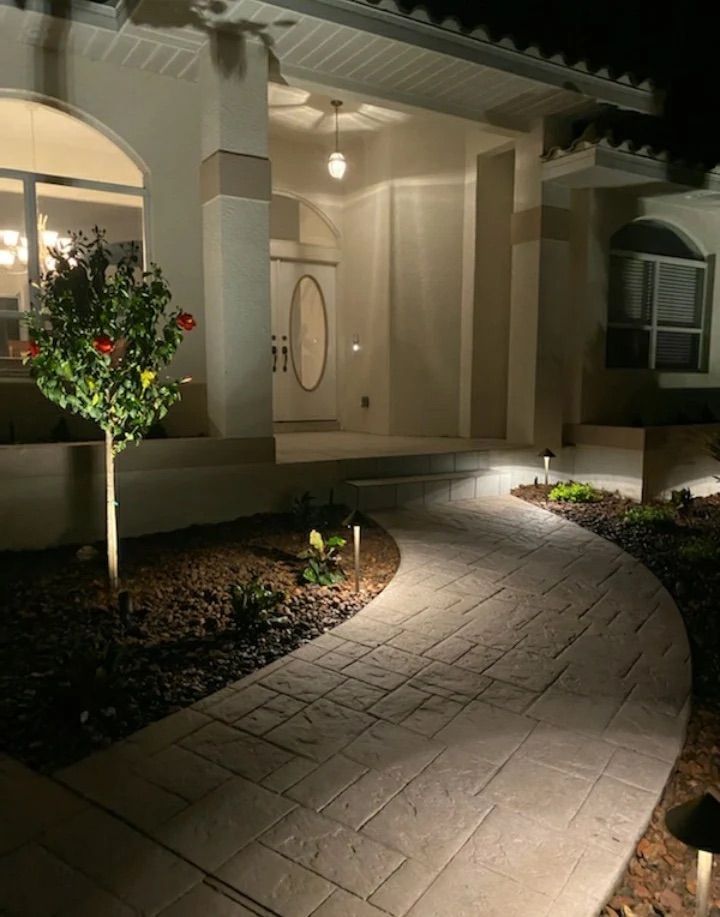 Curved stone walkway lit at night leading to a warmly lit front porch and front door