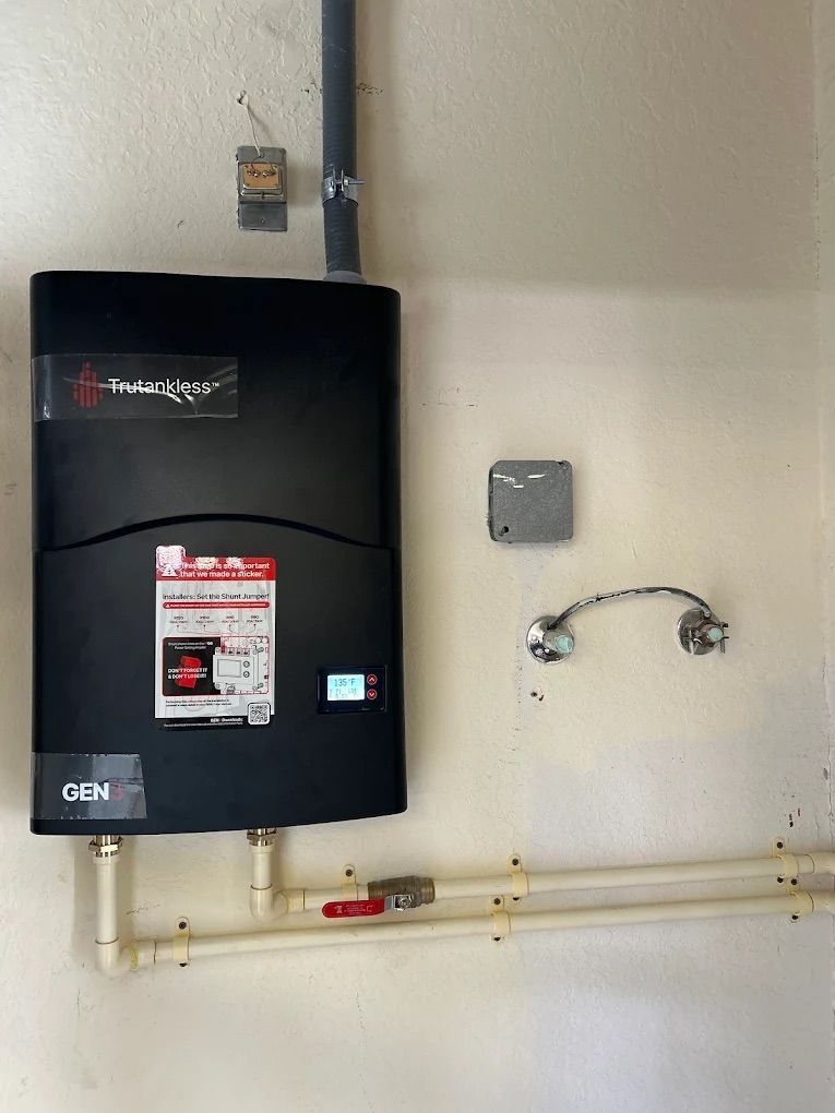 Black wall-mounted box and plumbing pipes on a light wall, with a small square panel and cable.