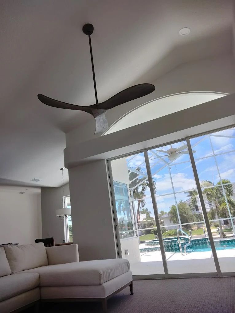 Bright living room with white sofa, modern ceiling fan, and large sliding glass doors to a pool outside