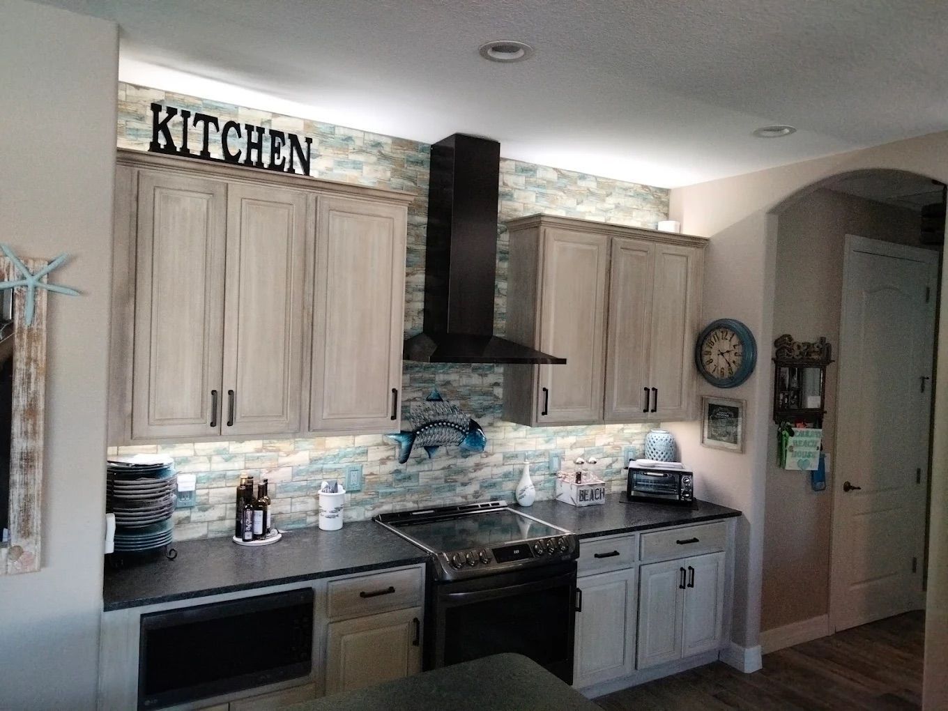 Kitchen with light wood cabinets, black stove hood, and granite countertops in a bright, modern room