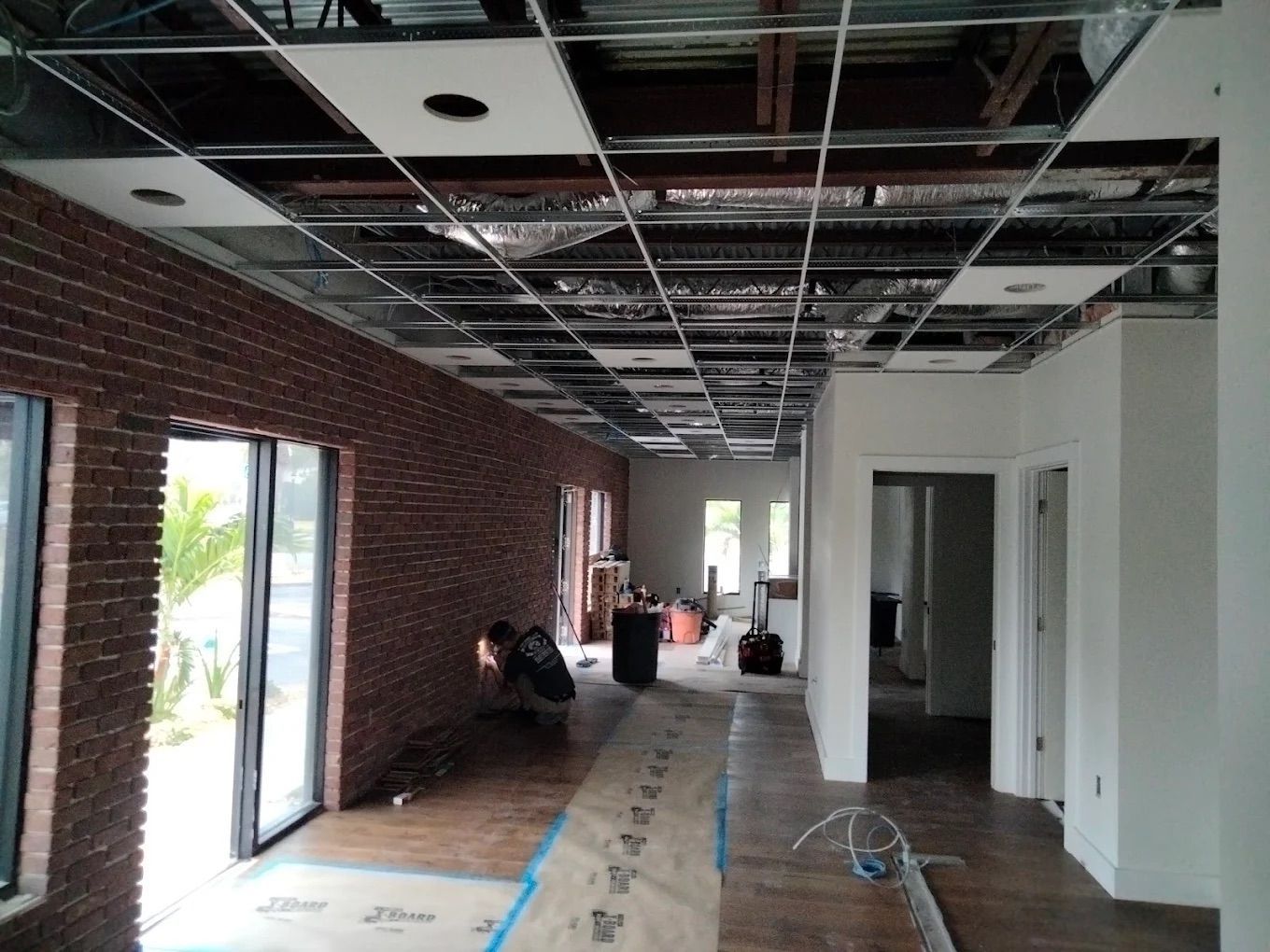 Interior of a building under renovation with exposed ceiling, brick wall, and unfinished hallway.