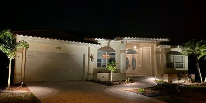 Well-lit single-story house exterior at night with garage, front door, and landscaped entryway
