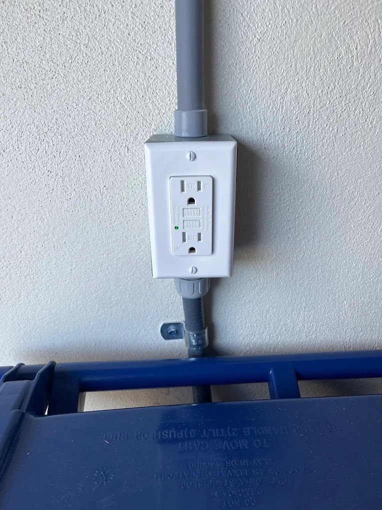 Wall-mounted GFCI outlet with gray conduit above a blue utility bin