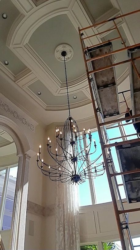 Grand hall ceiling with ornate chandelier and scaffolding beside tall windows