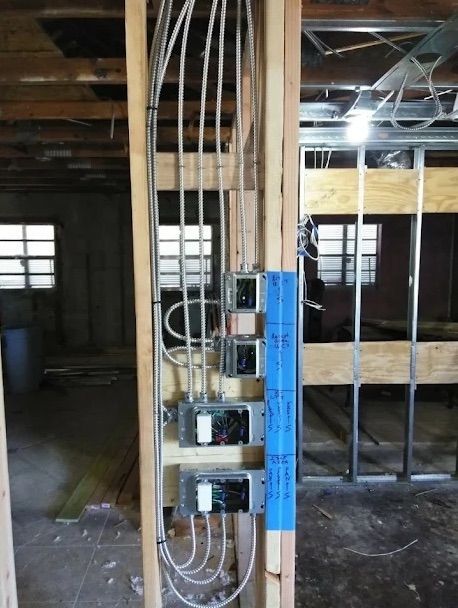 Electrical wiring and breaker boxes mounted on exposed studs in an unfinished room.