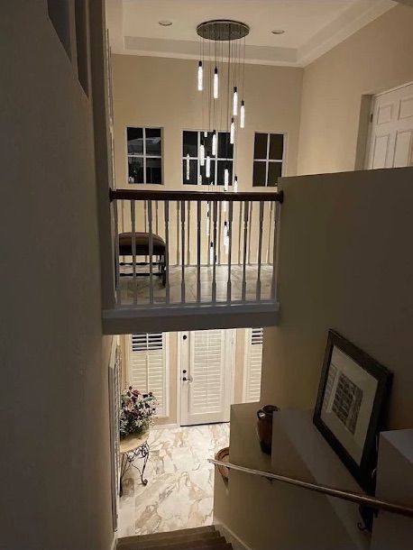 Stair landing overlooking a foyer with a hanging chandelier, railing, and framed art on beige walls