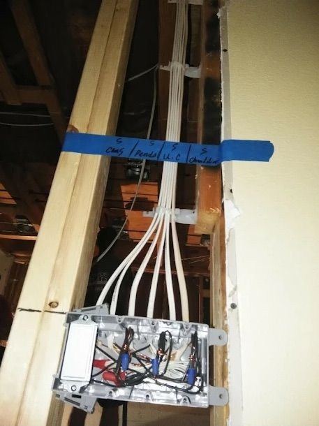 Electrical wiring and junction box mounted on exposed wall framing, secured with blue tape.