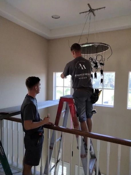 Two workers on ladders installing a ceiling light in a beige stairwell