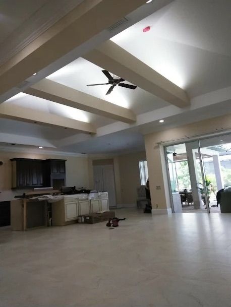 Bright open living room with kitchen, exposed beams, ceiling fan, and sliding glass doors to a patio.