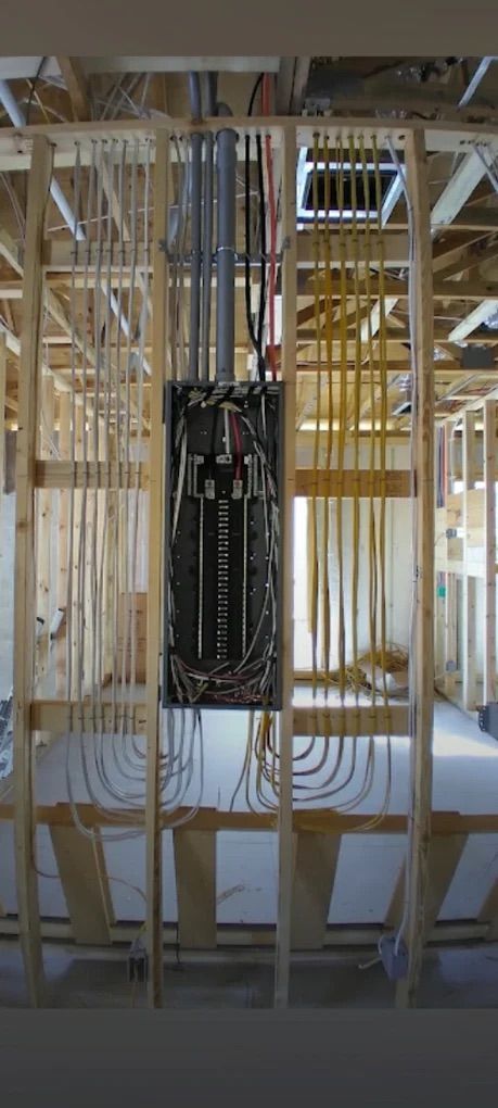 Framed house interior with exposed studs, electrical wiring, and central breaker panel under construction