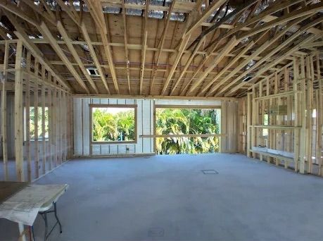 Unfinished house interior with exposed wooden framing, concrete floor, and large window openings.