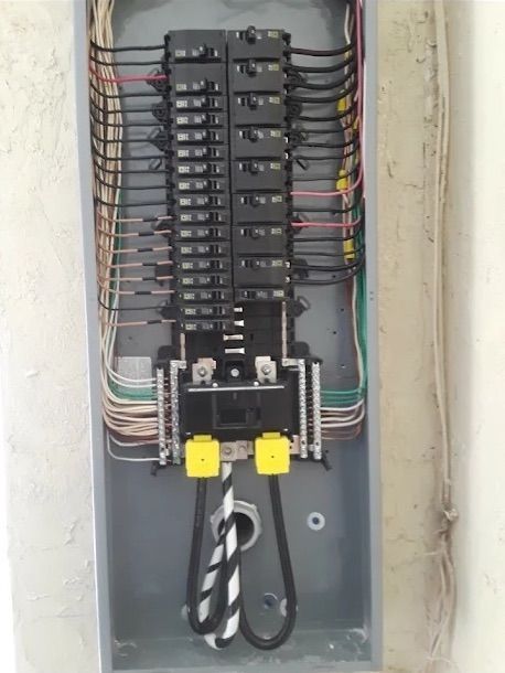 Electrical breaker panel with rows of circuit breakers and colored wires in a metal box.