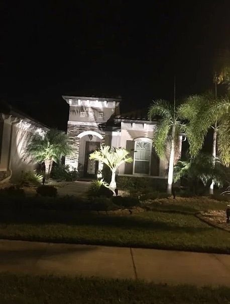 Nighttime view of a lit suburban house with palm trees and a front lawn