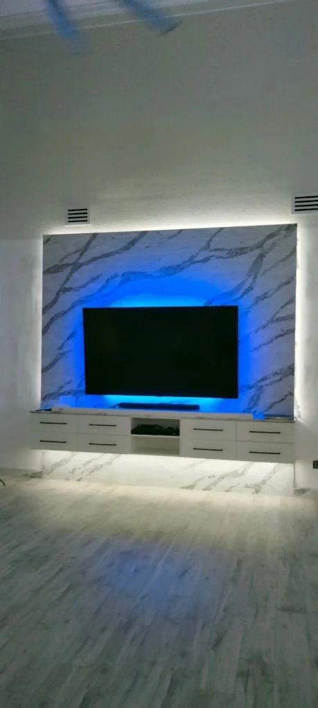 Modern TV wall with blue LED backlighting and white marble-style paneling in a bright room