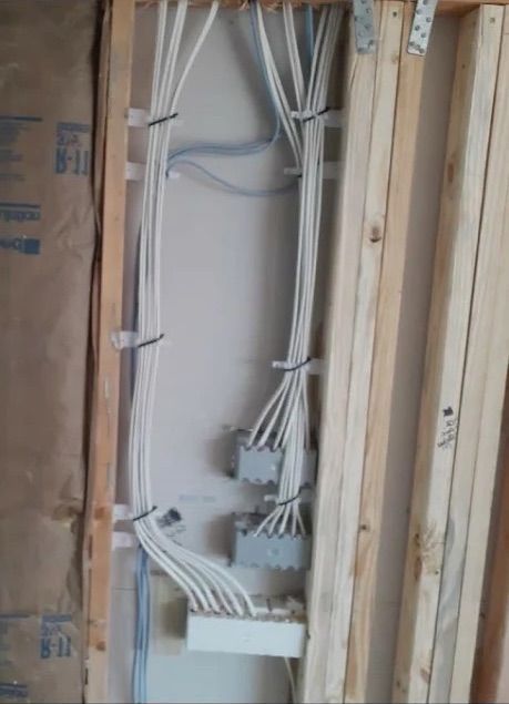 Electrical wiring and breaker panel inside an unfinished wall frame.