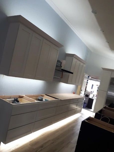 Modern kitchen with gray cabinets, white counters, and under-cabinet lighting along a long wall.