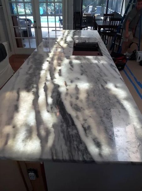 Marble countertop with an inset sink in a sunlit kitchen, showing tree shadows across the surface.