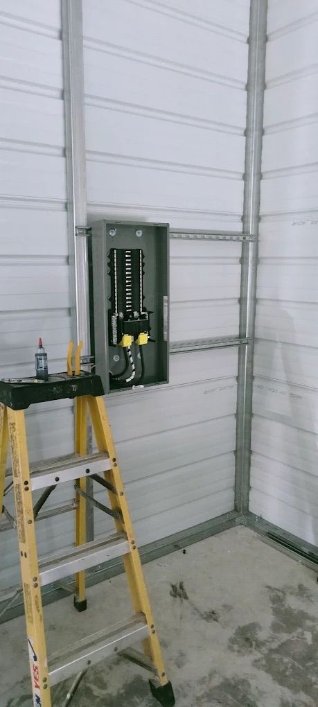 Open electrical panel on warehouse wall beside a yellow step ladder