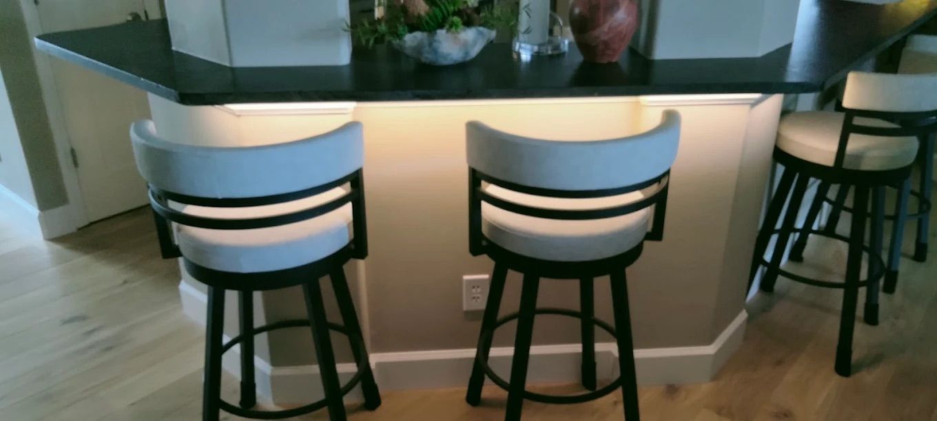 Modern bar counter with three black stools and warm underlighting in a contemporary room