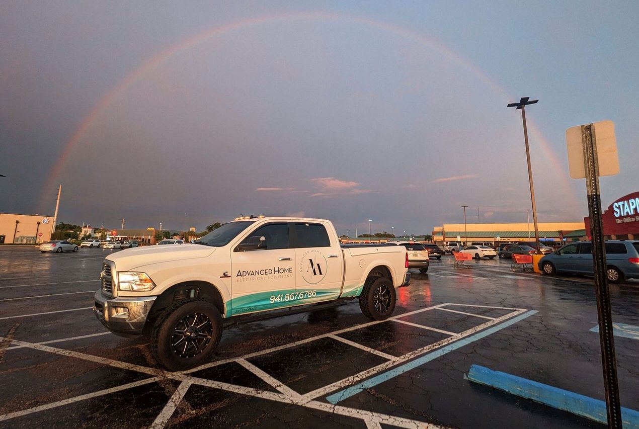 White pickup truck in a wet parking lot at sunset with a rainbow in the sky.