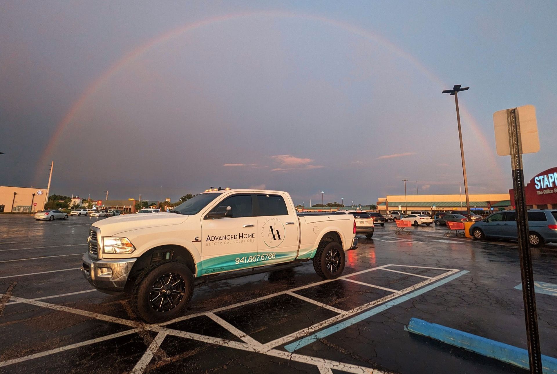 White pickup truck in a wet parking lot at sunset with a rainbow in the sky.