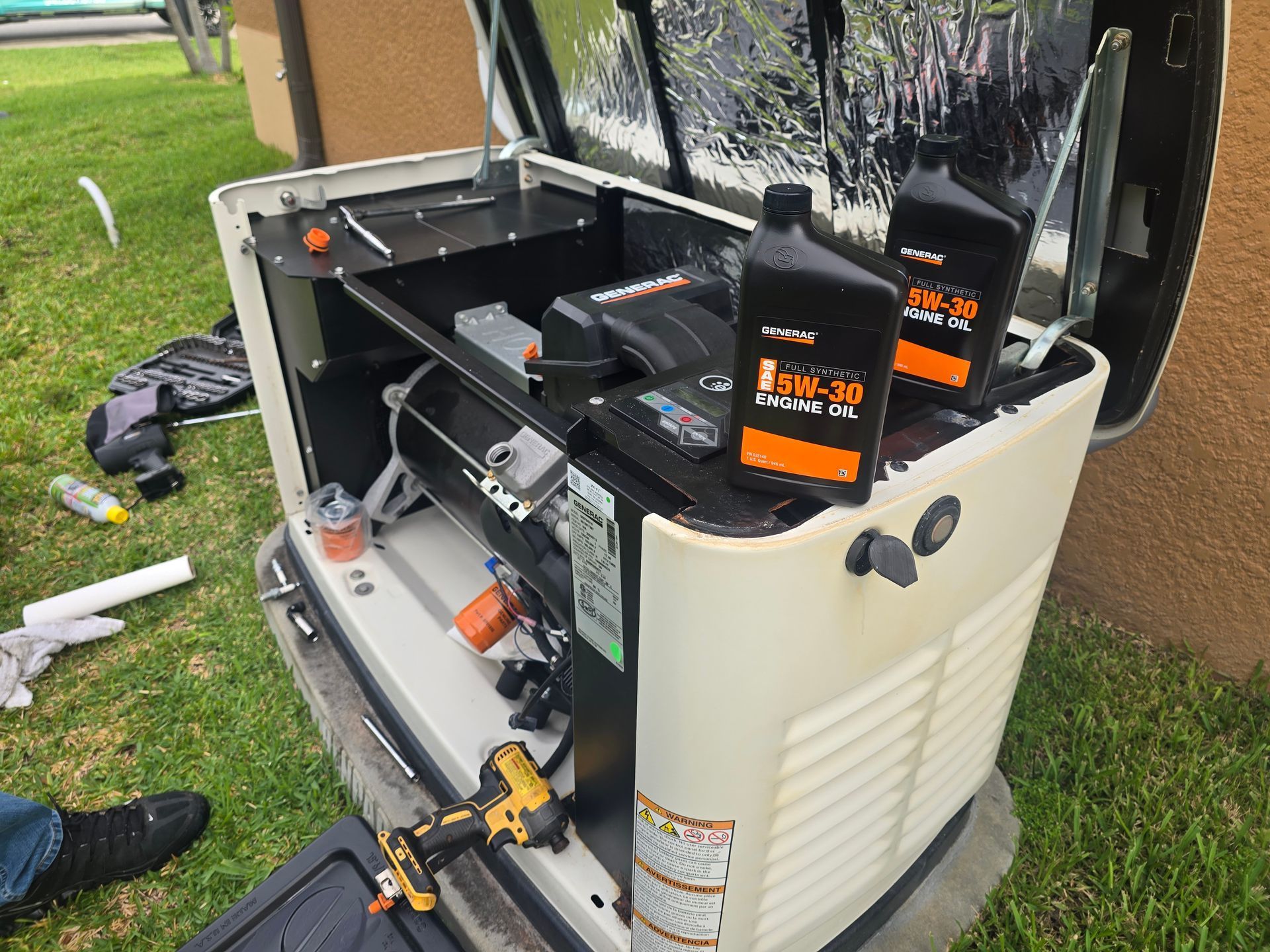 Open outdoor generator with tools and oil bottles on top, sitting on grass near a house.