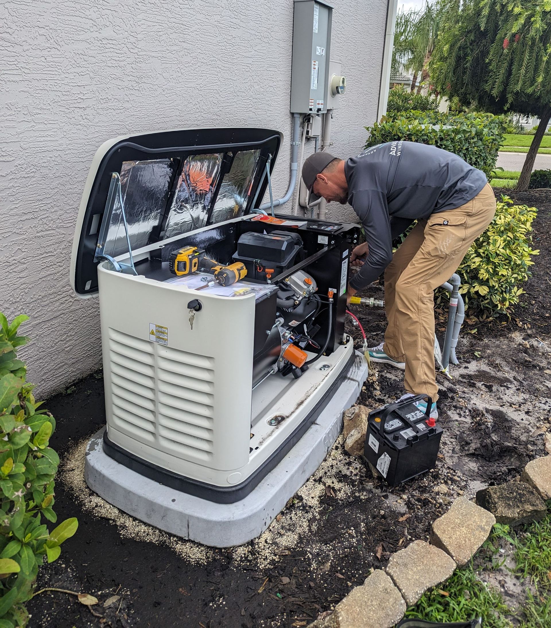 Technician inspecting an open home generator beside a house, with tools and a wet yard nearby.