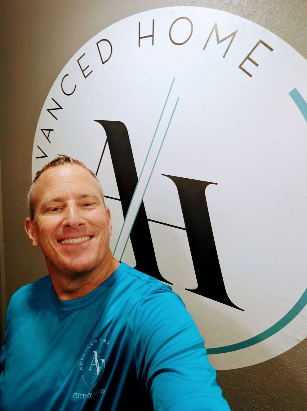 Smiling man in a blue shirt posing in front of an Advanced Home logo wall