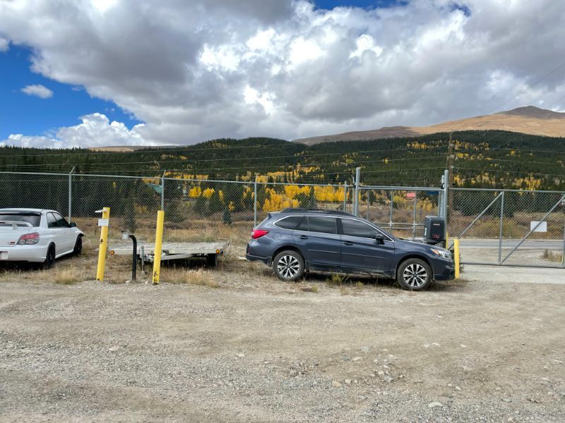 A care is parked in a gravel lot next to a fence.
