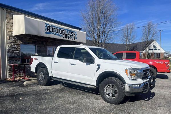 A white pickup truck is parked in front of a car dealership.
