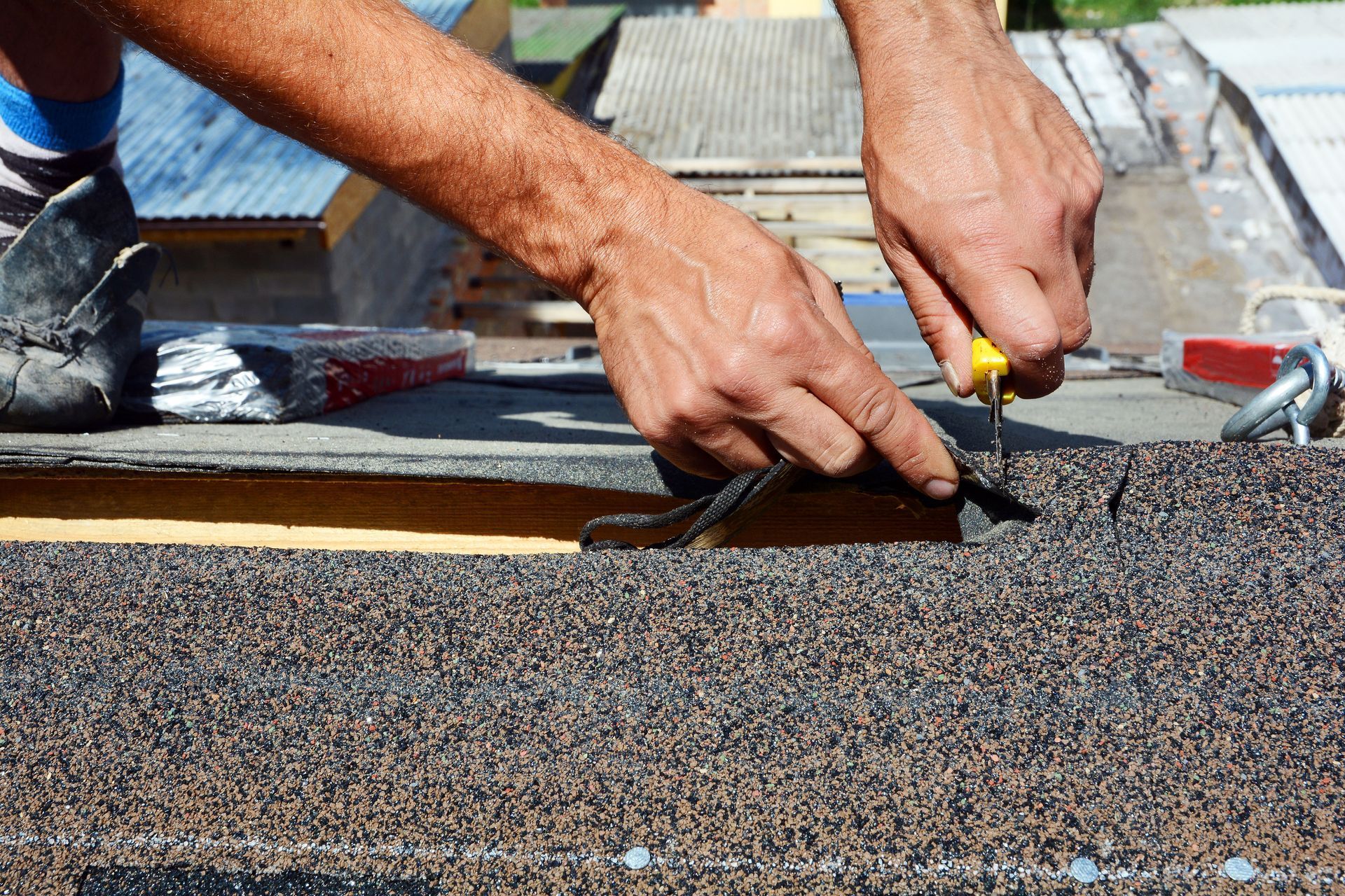Hands of a person using a tool to repair a roof with brown shingles.