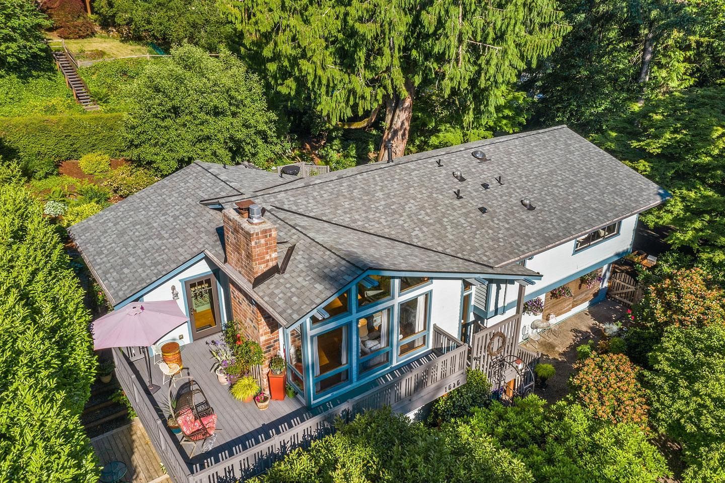 Aerial view of a gray-roofed house with a deck surrounded by lush green trees.