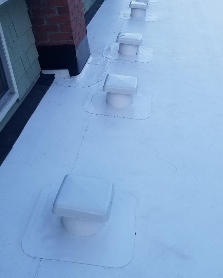 White flat roof with several ventilation pipes extending upward. A brick chimney is also present.