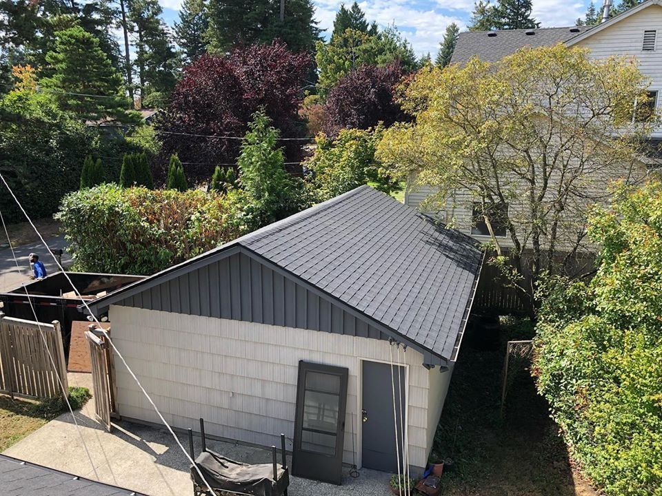 Gray-roofed garage surrounded by trees and bushes on a sunny day.