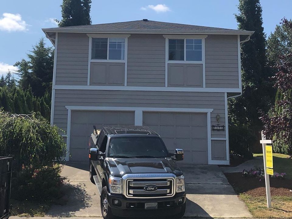 Two-story gray house with white trim; a black truck is parked in front of the garage.