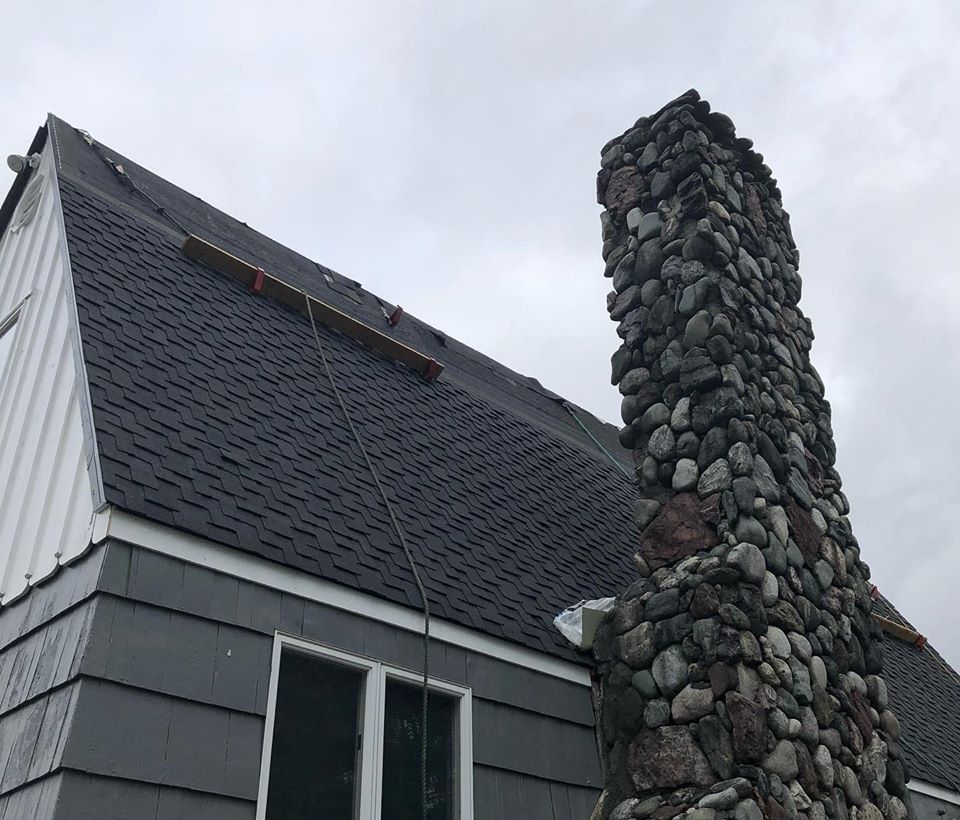 Gray house with dark roof and stone chimney under a cloudy sky.