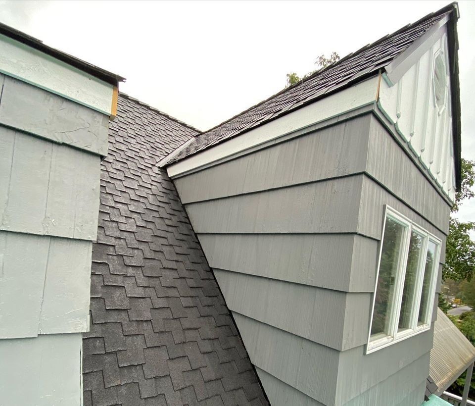 Gray shingled roof with a gray clapboard wall, white-framed windows, and a decorative circular element.